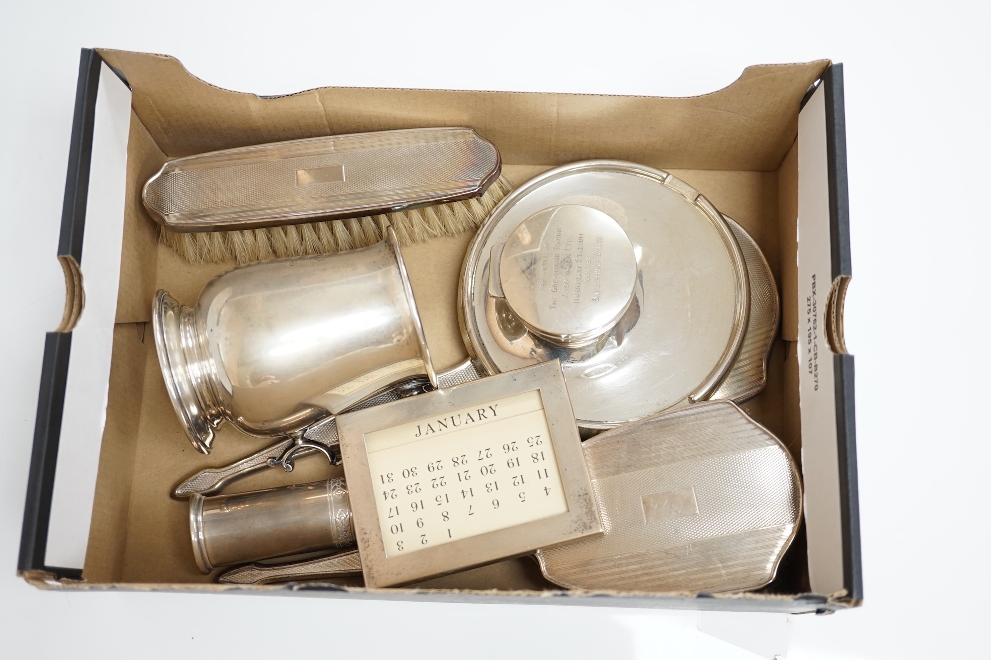 An Elizabeth II silver christening mug, three silver mounted dressing table items, a silver mounted desk calendar, a silver capstan inkwell and a sterling condiment. Condition - fair to good